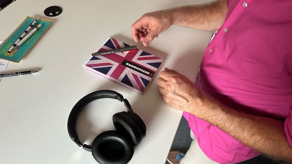 Hände halten eine Karte mit britischer Flagge, daneben Studiokopfhörer