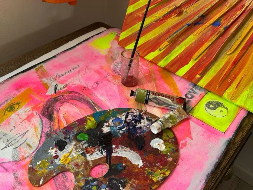 Farbpalette, Pinsel und Farbtuben auf einer pinken Leinwand im Atelier