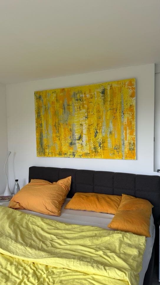 Das gelbe Bild über einem Bett mit orangen Kissen