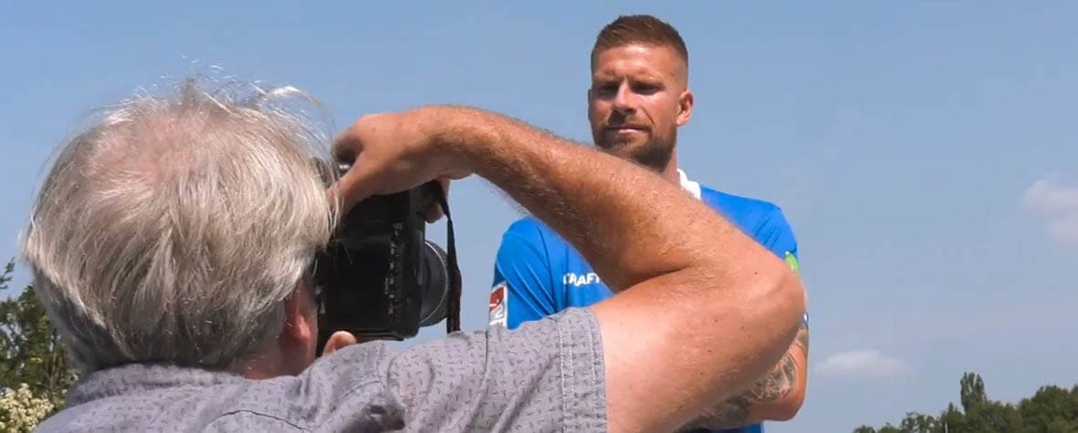 Nahaufnahme: Mitsch Schulz mit Kamera vor einem Spieler im blauen Trikot