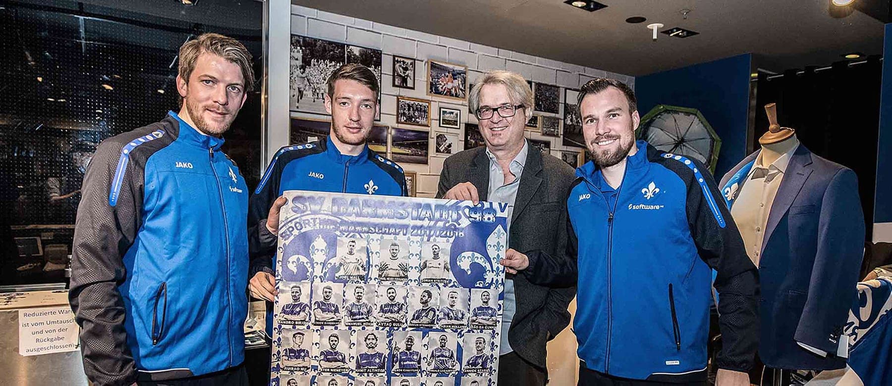 Spieler in Lilien-Trainingsjacken präsentieren mit Mitsch Schulz das Mannschaftsposter