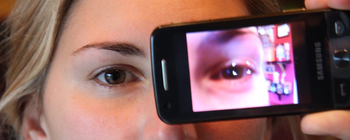 Eine Frau hält ein Handy vor ihr Auge, auf dem Display ist ihr Auge zu sehen